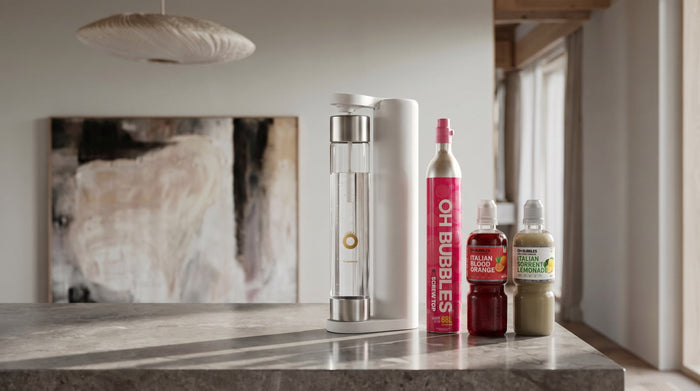 The white ALLFIZZ soda maker centred on a stone kitchen bench with the OH Bubbles CO2 cylinder, blood orange and Sorrento lemonade syrups beside it